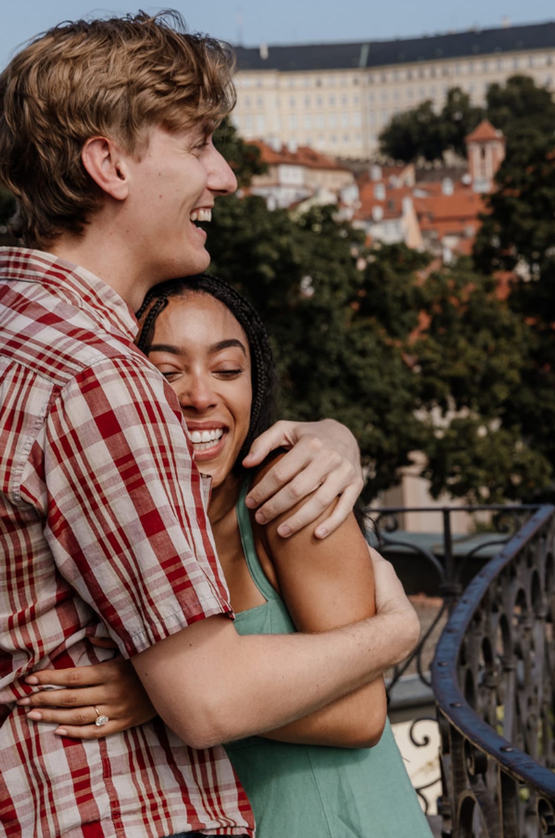 Newly engaged couple embracing on the Vrtba Garden terrace with Prague Castle behind