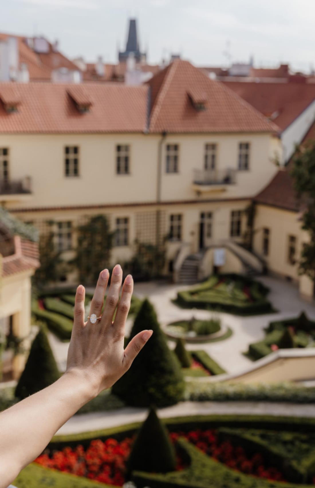 Engagement ring held up over the baroque parterre of Vrtba Garden, Prague